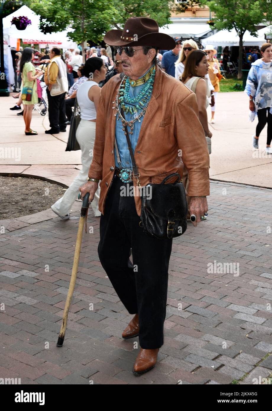 A man dressed in western clothing and wearing Native American jewelry walks through the histoici Plaza in Santa Fe, New Mexico. Stock Photo