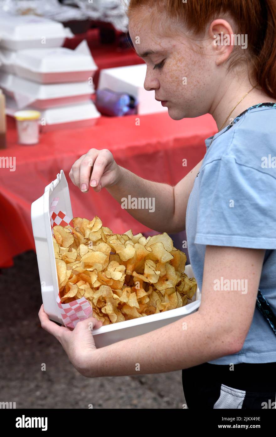 A young girl purchases a carton of ribbon fries from a food vendor at an outdoor festival in Santa Fe, New Mexico. Stock Photo
