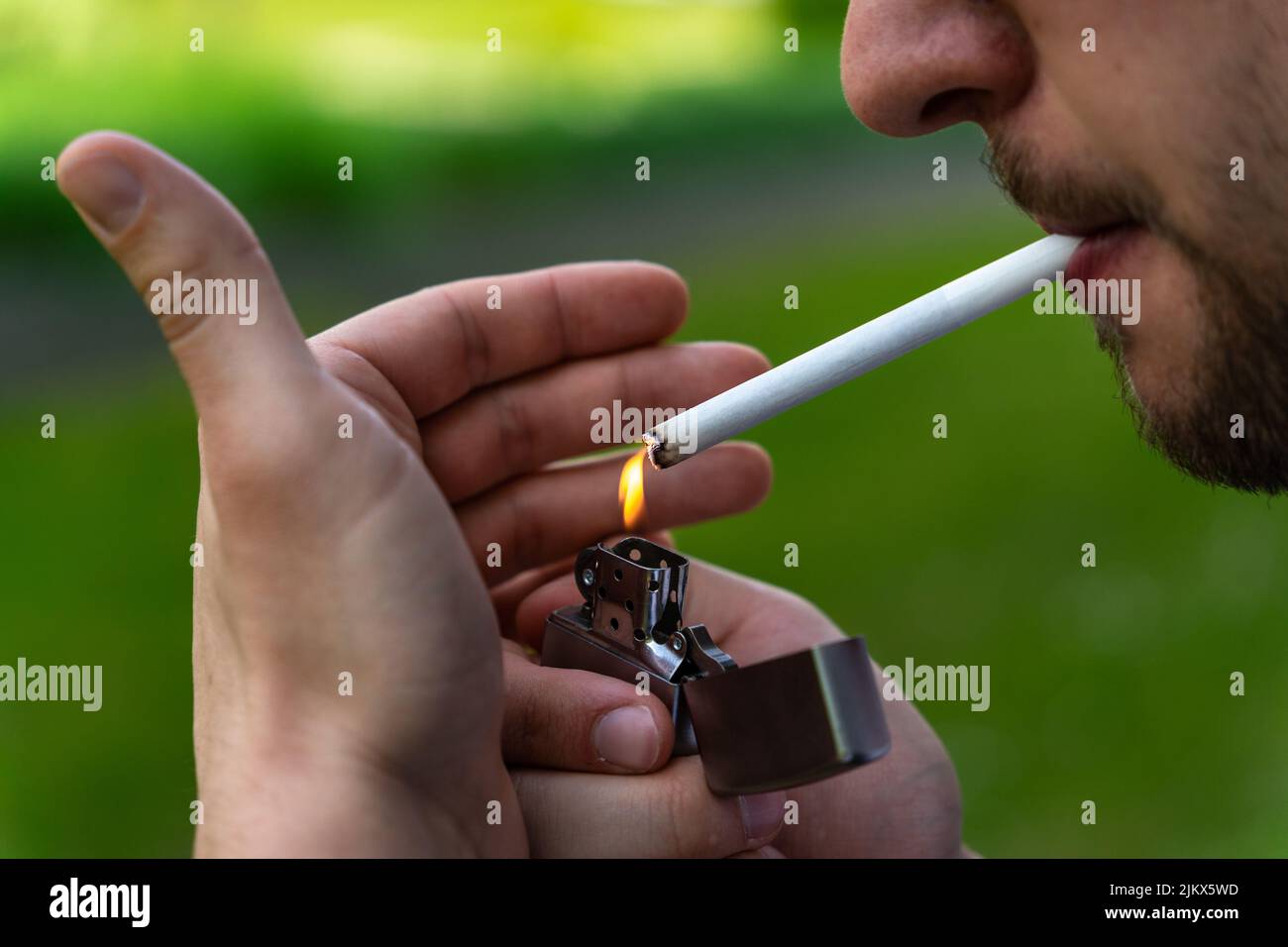 Young bearded man lighting a cigarette with a metal lighter close up Stock Photo