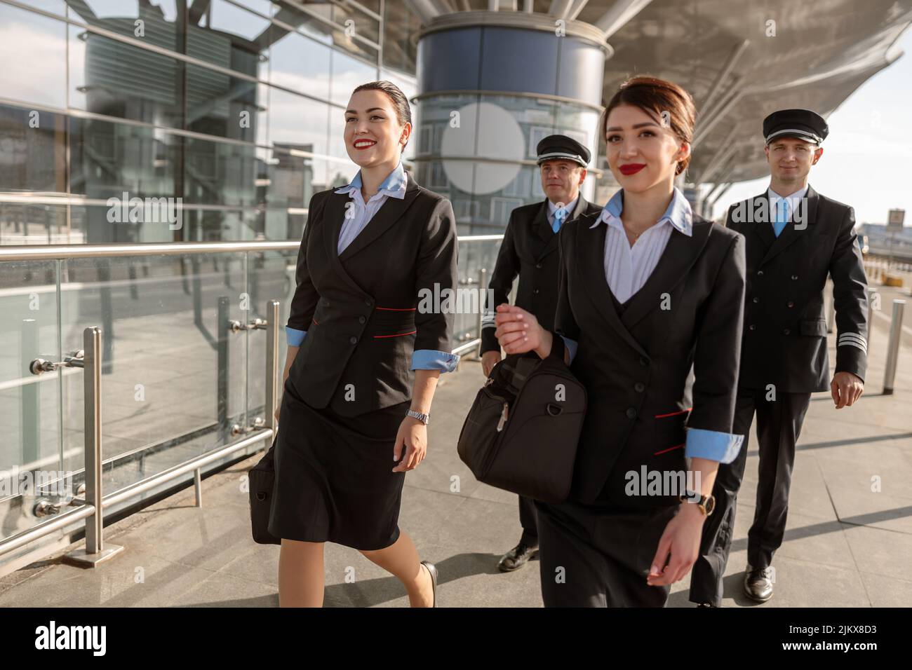 Happy pilots and stewardesses walking along the terminal outdoors Stock Photo