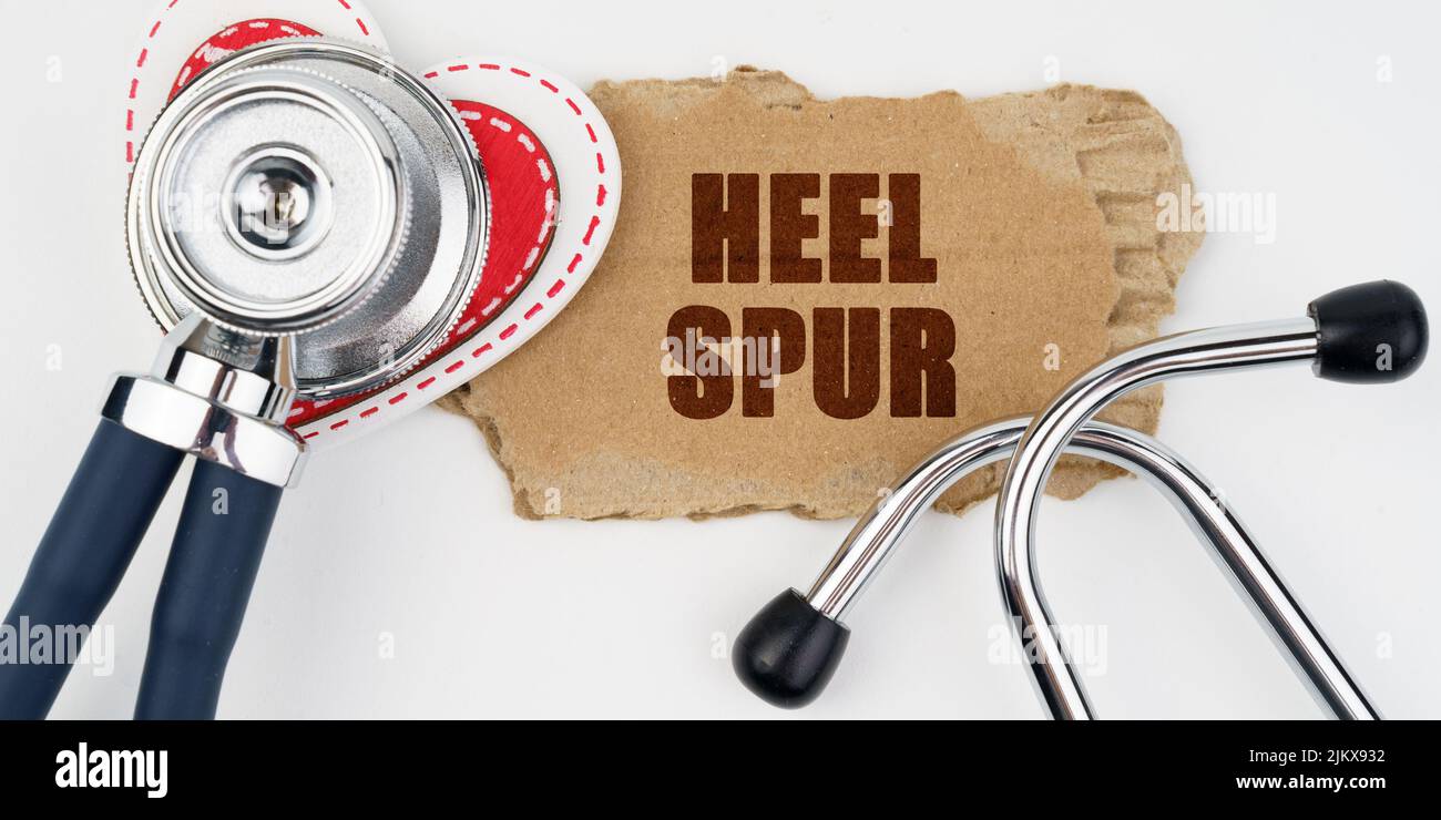 Medicine and health concept. On a white table lie a heart, a stethoscope and a cardboard with the inscription - Heel Spur Stock Photo
