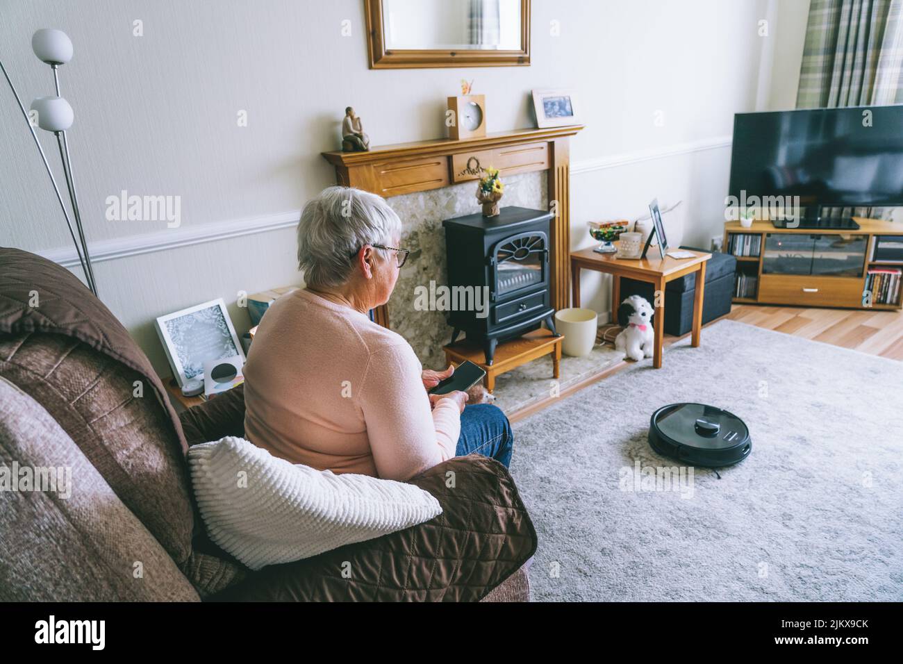 Senior woman using a robot vacuum cleaner through phone settings while