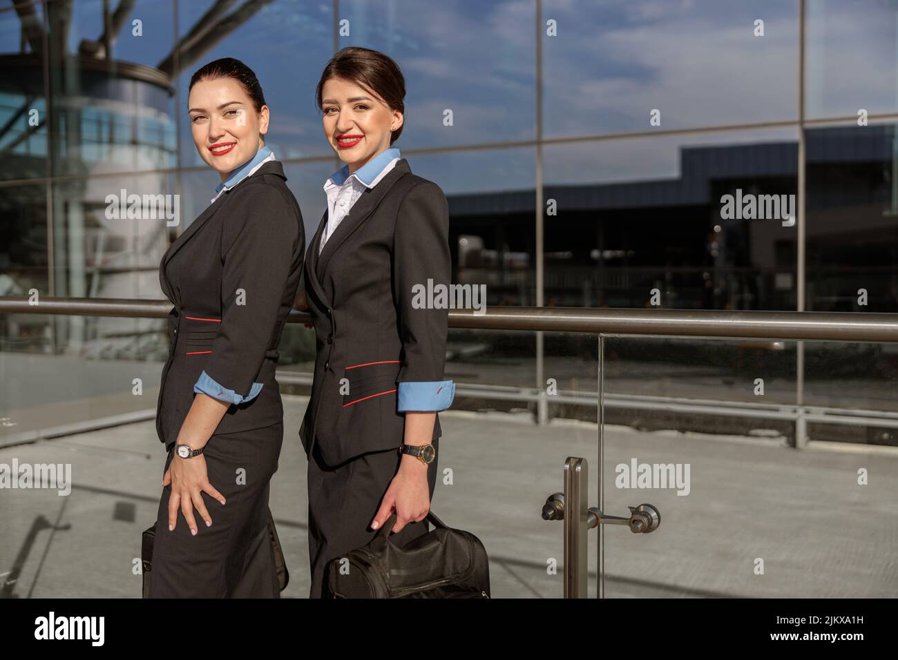 Happy flight attendants with hand luggage standing near terminal Stock Photo