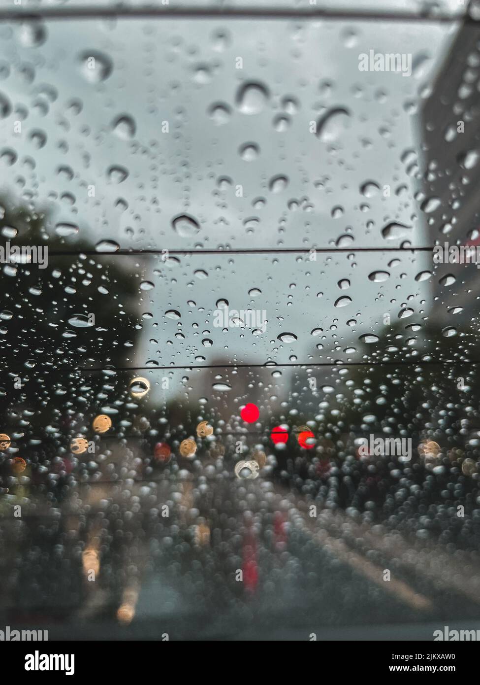 A vertical shot of raindrops on a car window with bokeh lights Stock