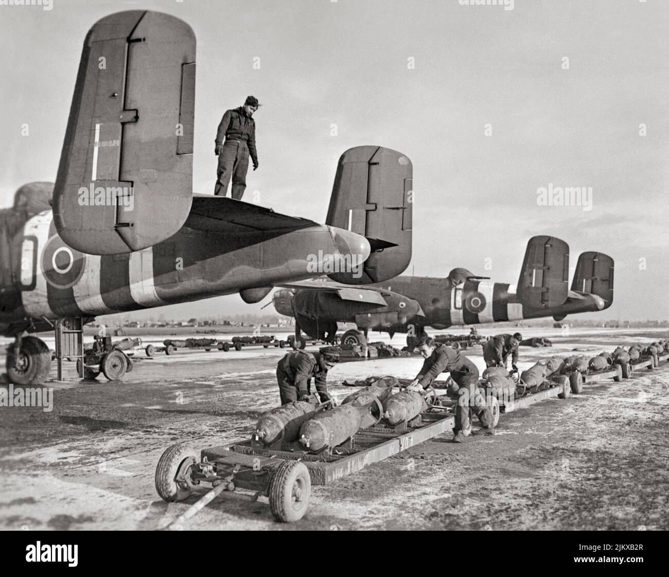 RAF and Dutch naval ground crews prepare to load 500-lb MC bombs into North American Mitchell Mark IIs of No. 98 Squadron RAF, during wintry conditions in Belgium. The North American B-25 Mitchell was a medium bomber introduced in 1941 and used by many Allied air forces. Stock Photo