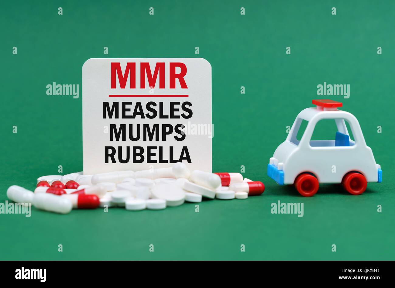 Medical concept. On a green surface, an ambulance, pills and a white sign with the inscription - Measles-Mumps-Rubella Stock Photo