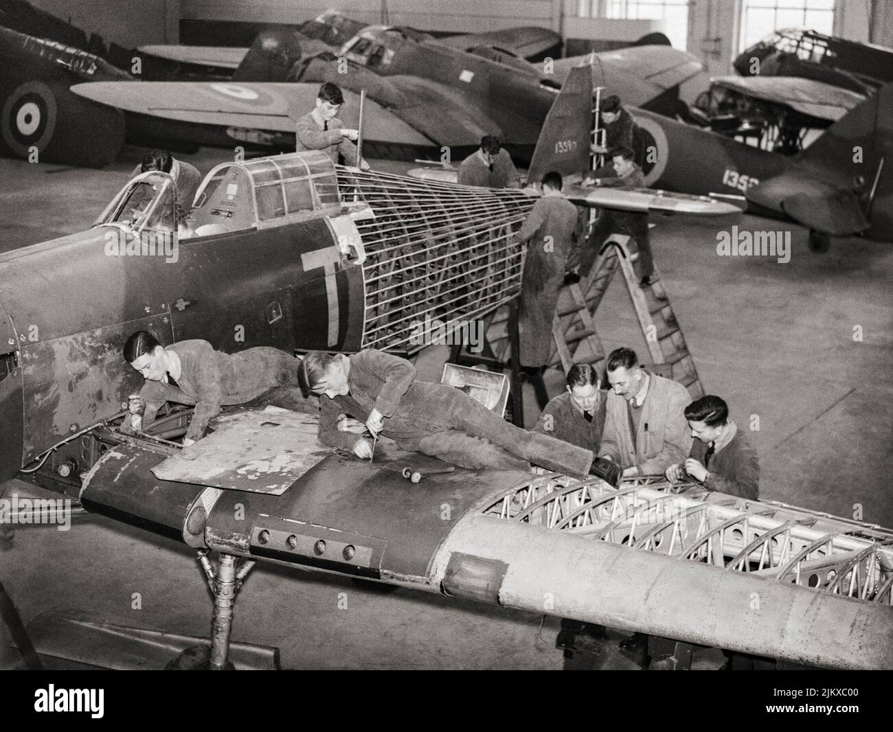 Trainee airframe fitters are taught repair procedures on Hawker Hurricane instructional airframe, 1359M, in a hangar at No. 2 School of Technical Training, Cosford, Shropshire, England. The Hurricane flew with No. 111 Squadron RAF before crashing during a forced landing in January 1939. More instructional airframes, including Bristol Blenheim Mark Is and a Fairey Battle, can be seen in the background. Stock Photo