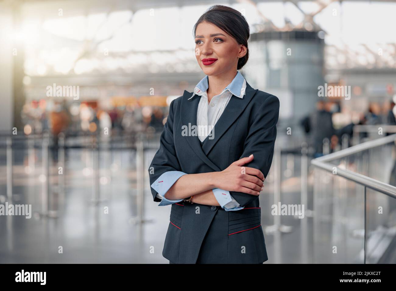 Beautiful stewardess with arms crossed looking away in airport terminal Stock Photo