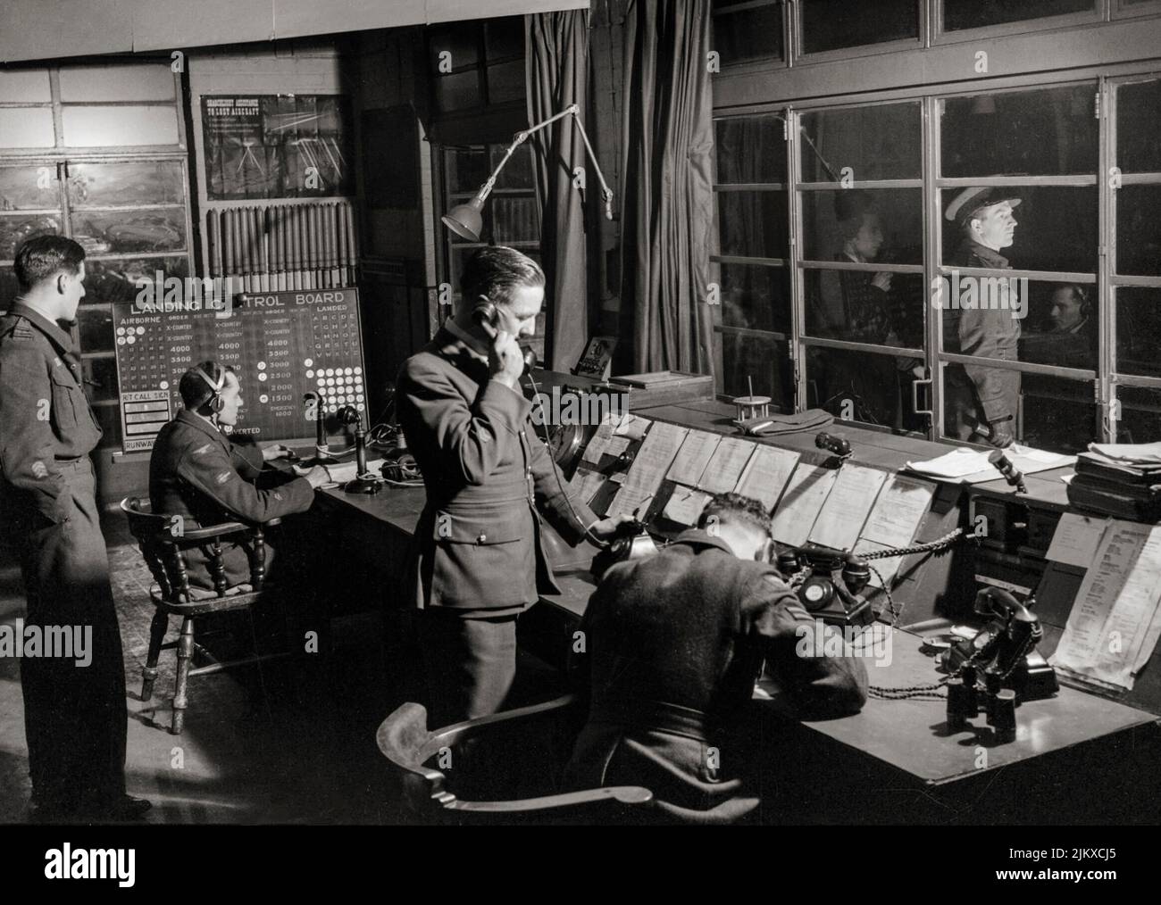 The Officer of the Watch in the Watch Office at Snaith, Yorkshire, England, guiding Handley Page Halifaxes of No. 51 Squadron RAF back to base after a night raid on Nuremberg. The Station Commander of Snaith, can be seen waiting outside on the balcony of the Control Tower. Stock Photo