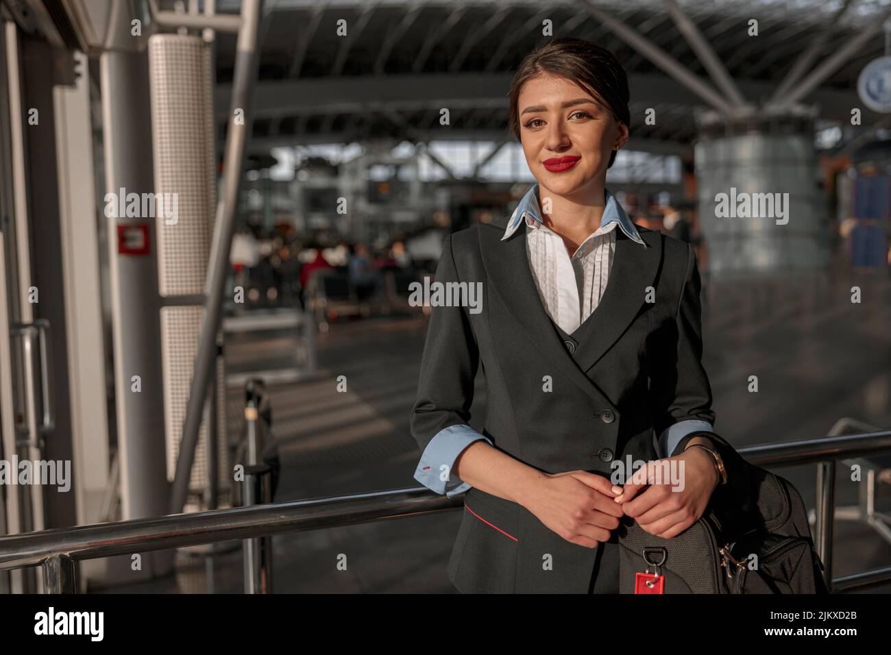 Smiling beautiful air hostess holding bag and posing at camera Stock Photo