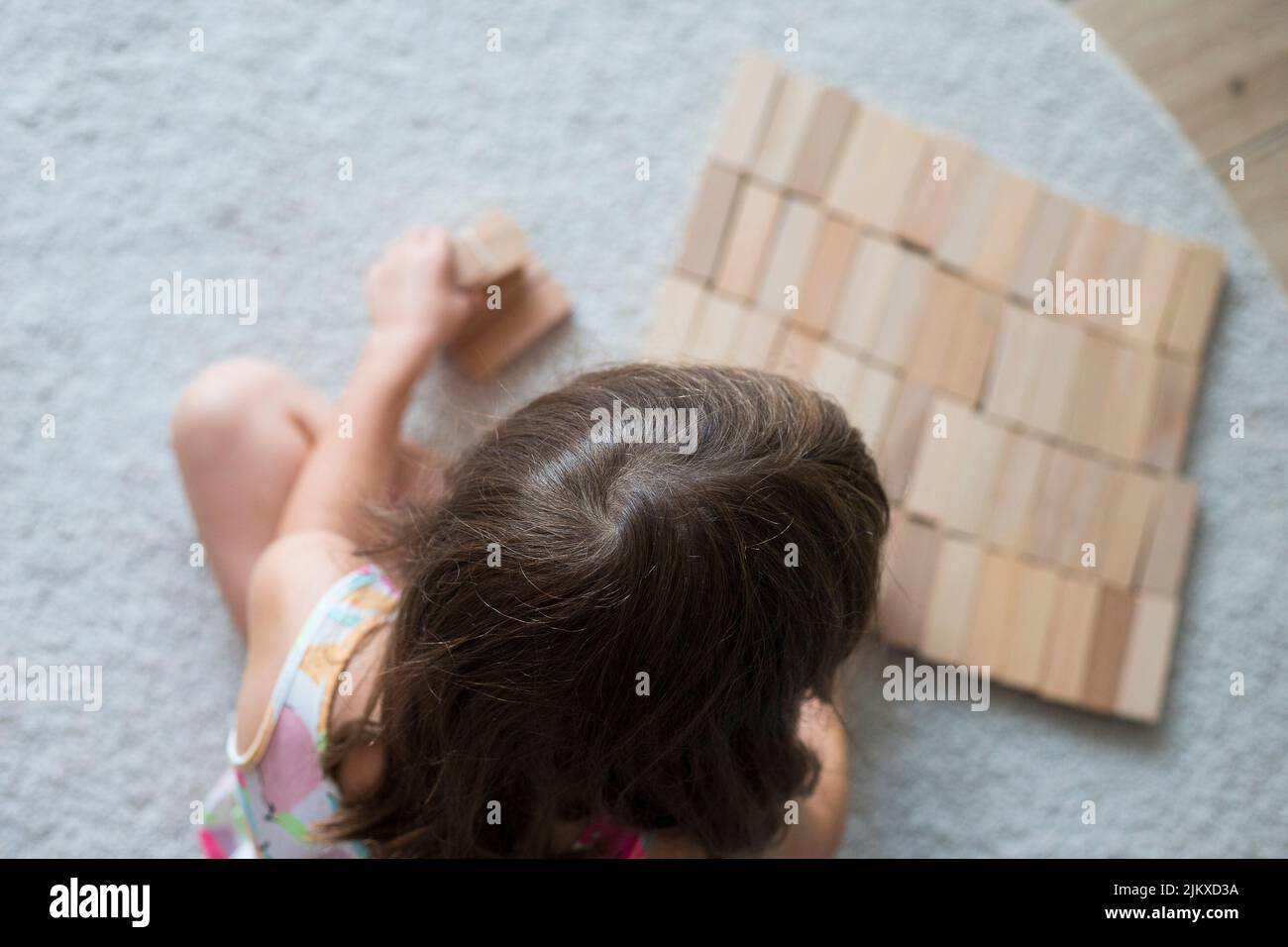 Caucasian child girl, 5 yers old, playing with wooden blocks on the floor, sitting on beige carpet indoor. Stock Photo