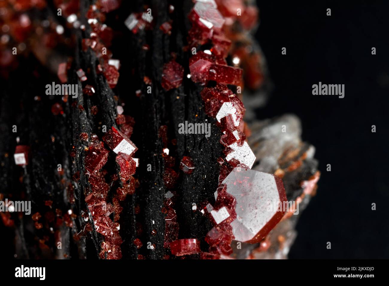 A closeup of small rare red minerals on a black blurred background Stock Photo