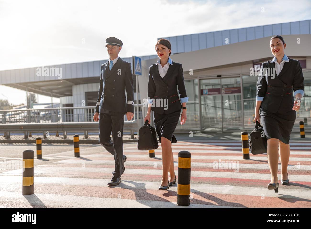 Two flight attendants with bags and their colleague crossing the road Stock Photo