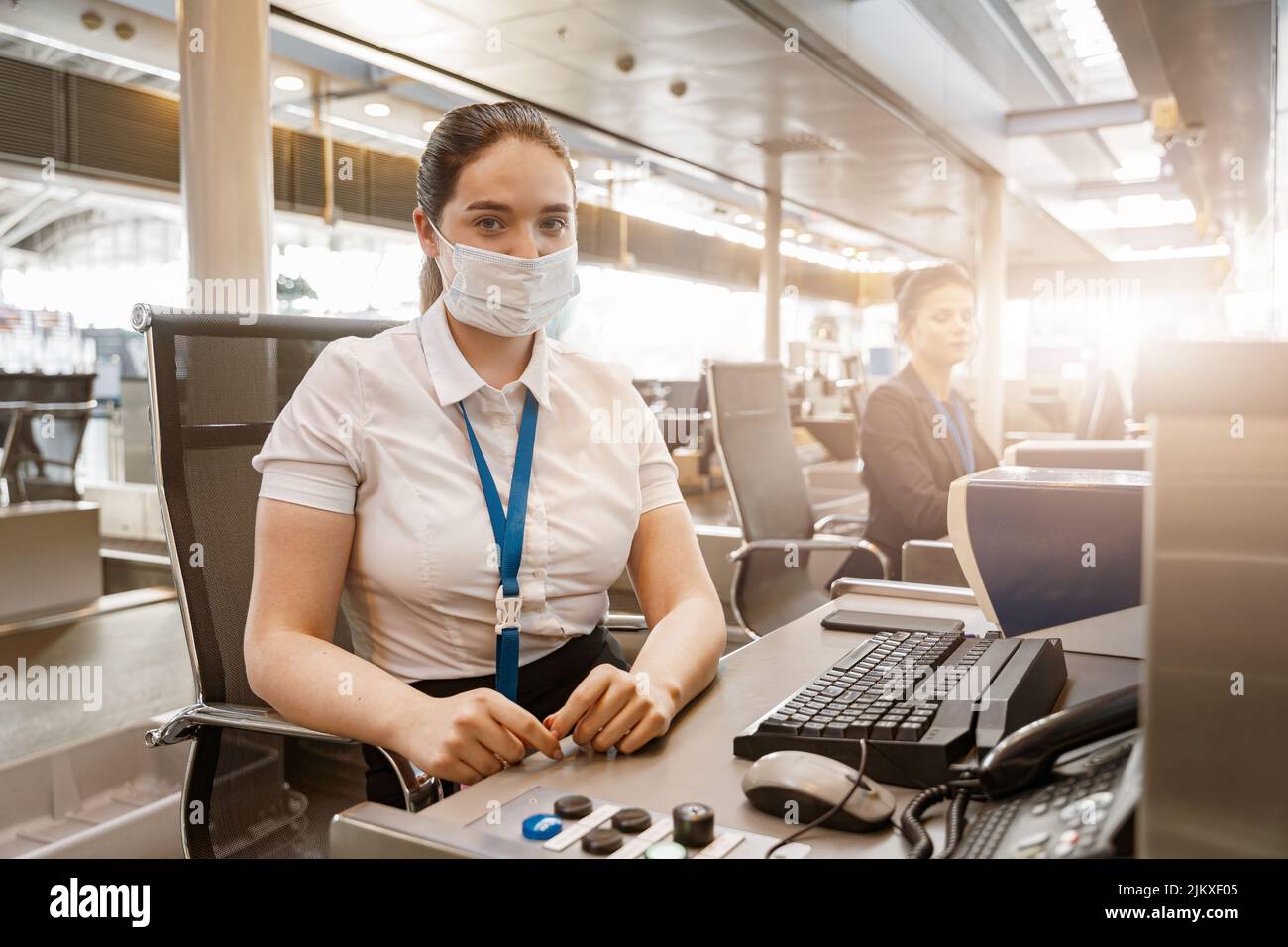 Woman airline employee wearing face mask while working at airline check in counter in airport Stock Photo