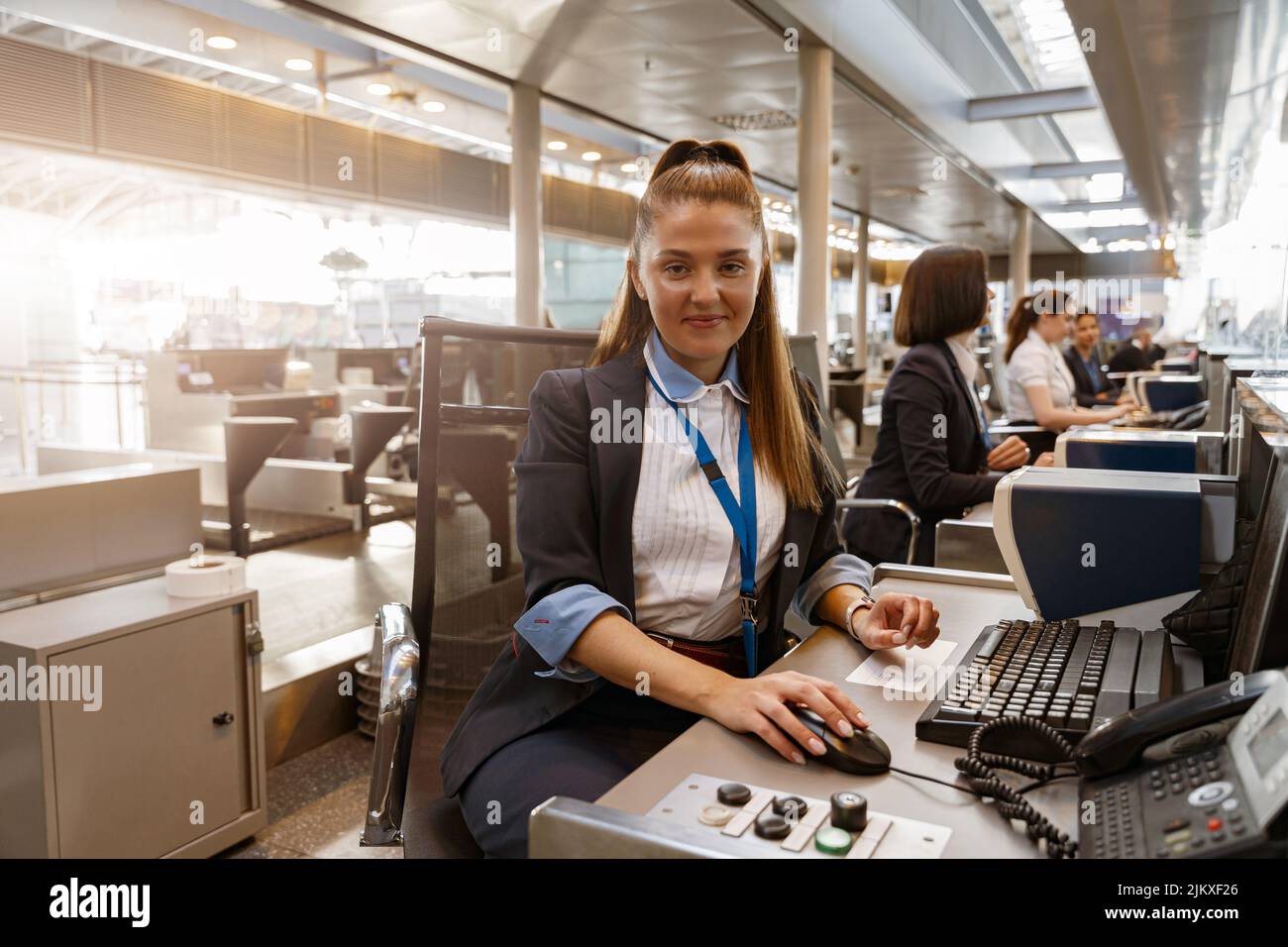 Woman airline employee working at airline check in counter in airport with colleagues on background Stock Photo