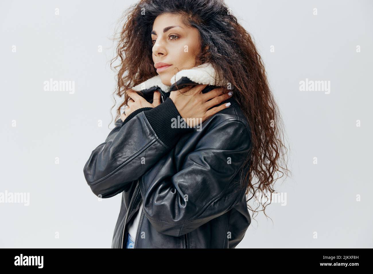 Thoughtful Curly Pretty Latin Lady Wrapping In Warm Leather Black Jacket With Fur Collar Looking Aside Posing Isolated At White Studio Background Stock Photo