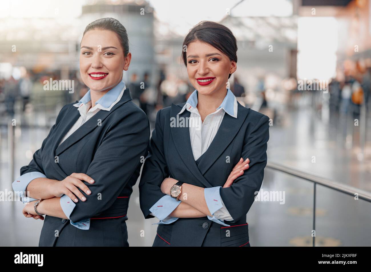 Smiling stewardesses with arms crossed standing in airport terminal Stock Photo