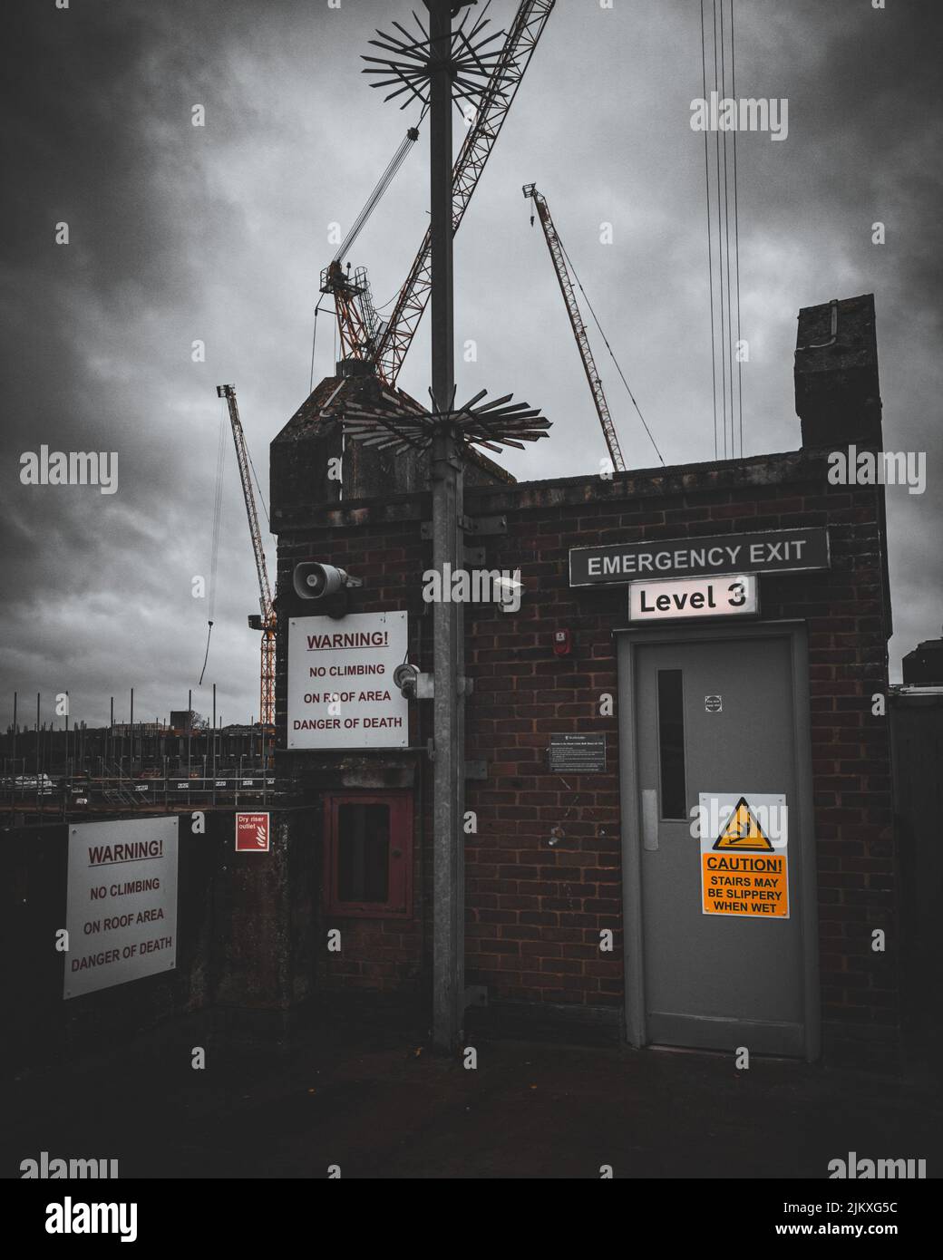 A vertical shot of a small building with warning signs with tall tower cranes in the background Stock Photo