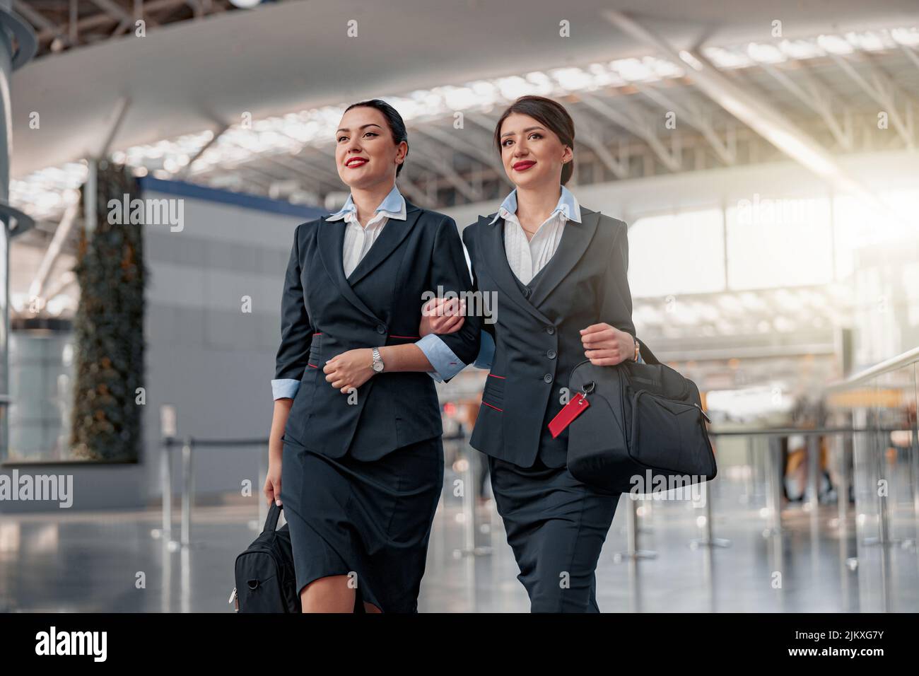 Smiling pretty flight attendants with bags walking through the terminal