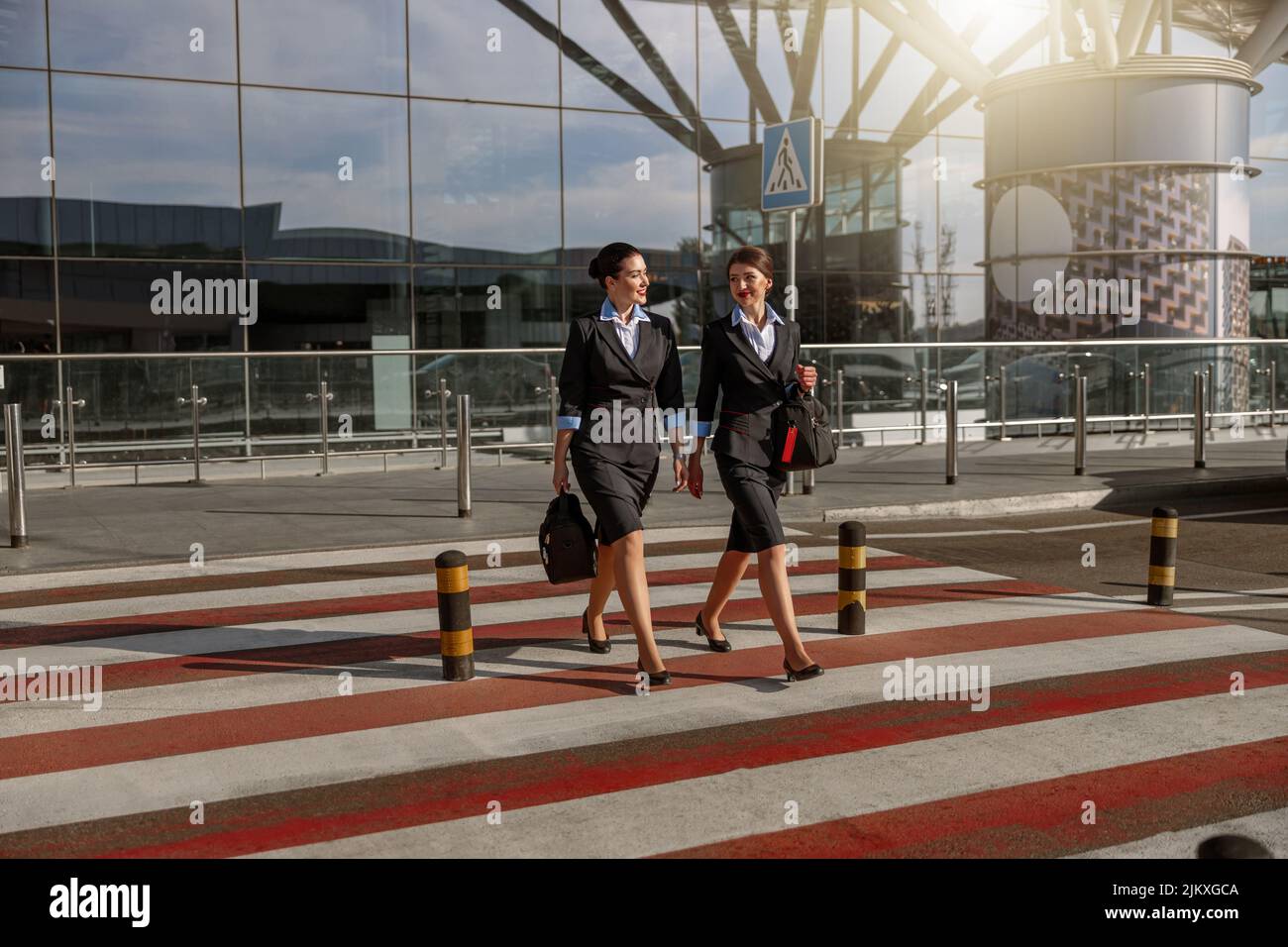 Happy pretty flight attendants with bags crossing the road outdoor Stock Photo