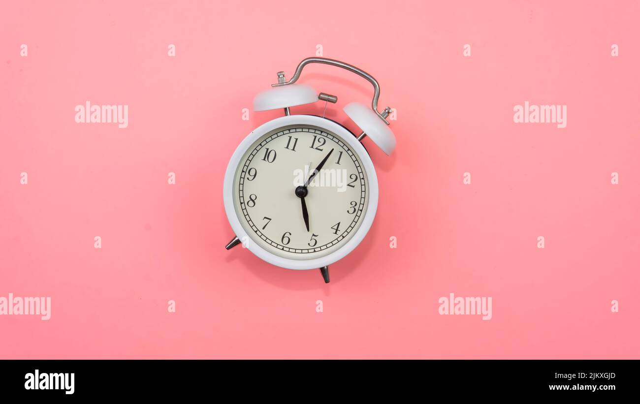 Selective focus on a white alarm clock on a pink background. A fallen white alarm clock showing how time cannot be wasted. Stock Photo