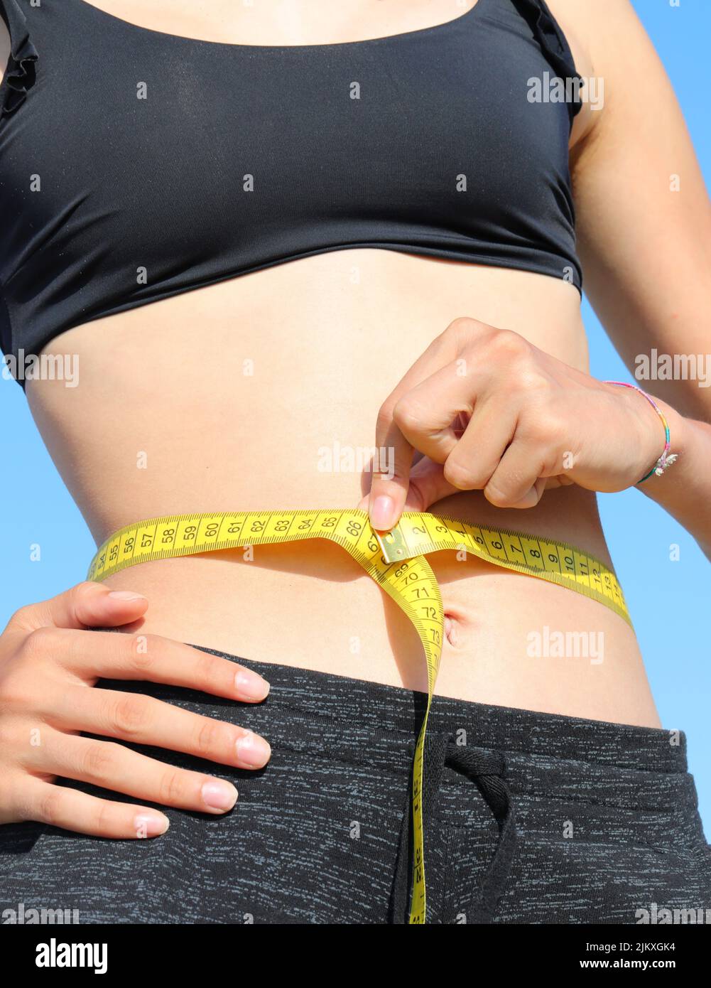 skinny girl measuring her waist using a yellow flexible tape measure with summer clothes Stock Photo