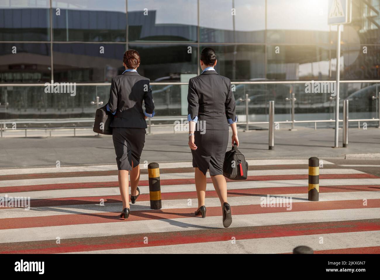 Two flight attendants with bags crossing the road near the airport terminal Stock Photo