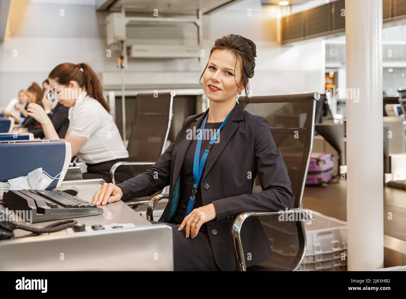 Woman airline employee working at airline check in counter in airport with colleagues on