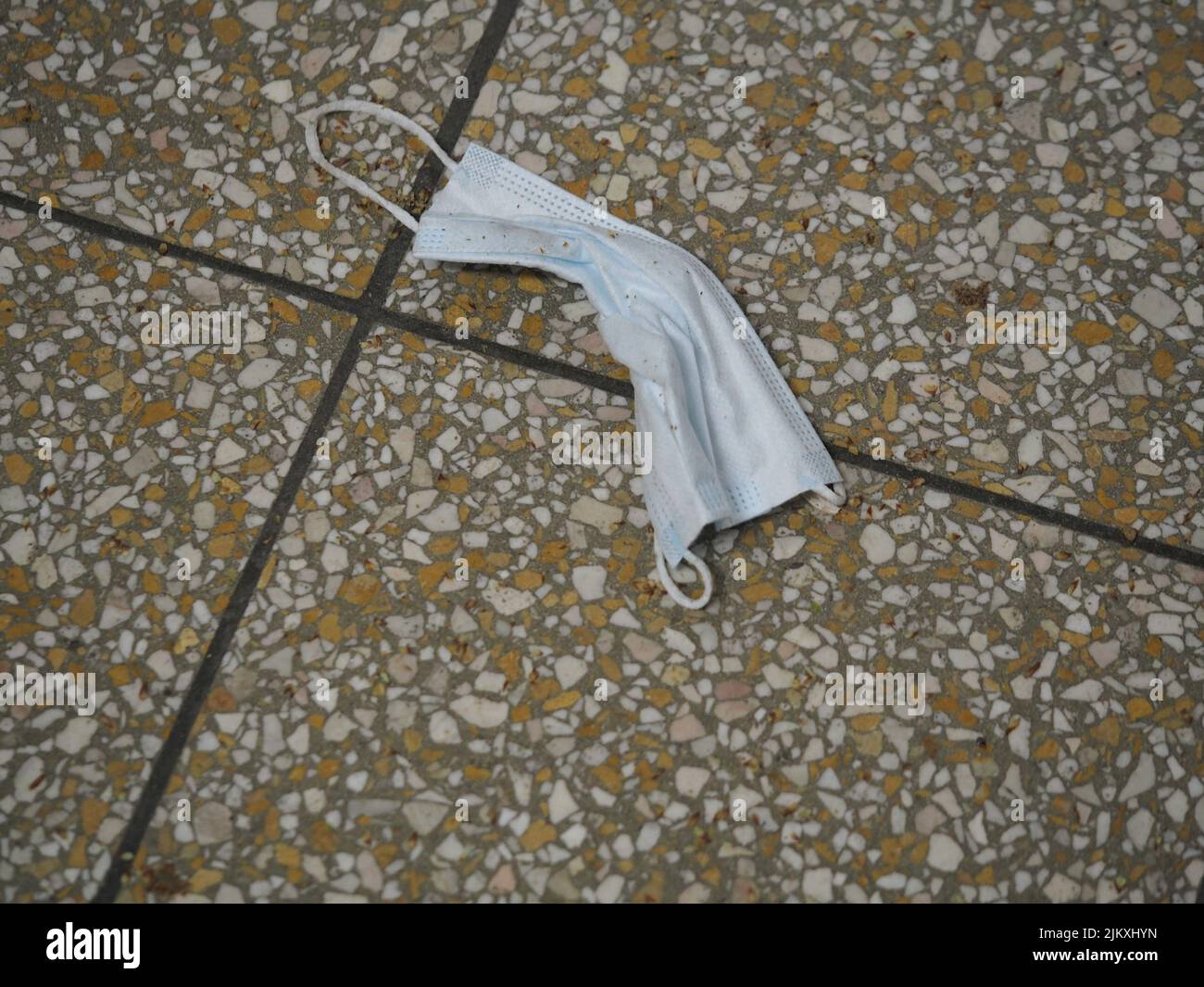 dirty used medical face mask laying on a tile floor in a central station Stock Photo