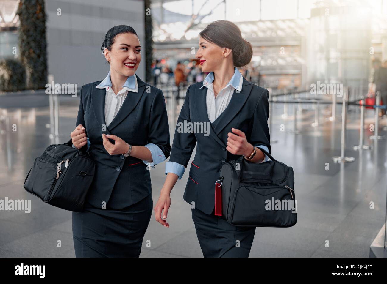 Smiling pretty flight attendants with bags talking in the terminal Stock Photo