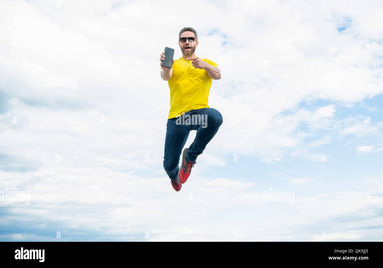 man jumping and presenting smartphone on sky background Stock Photo