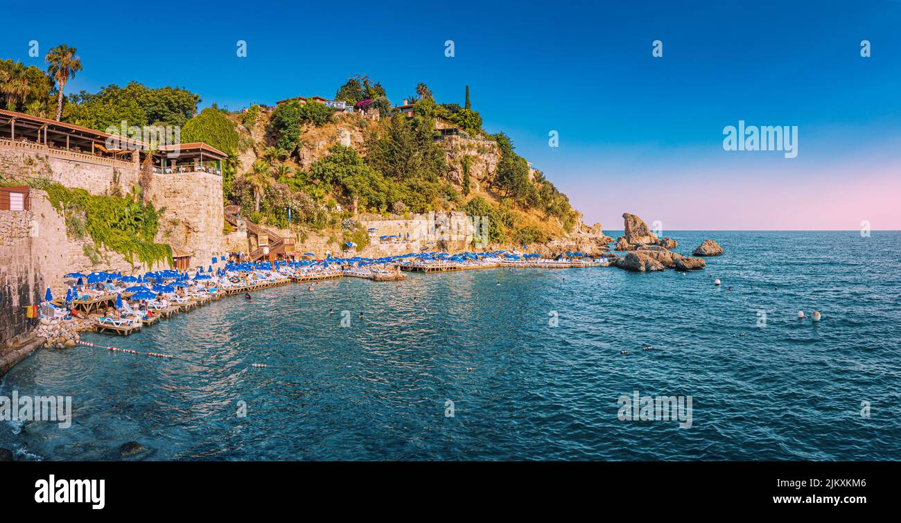 21 June 2022, Antalya, Turkey: Popular Mermerli beach with sun umbrellas and swimming and resting people near Antalya old town Stock Photo