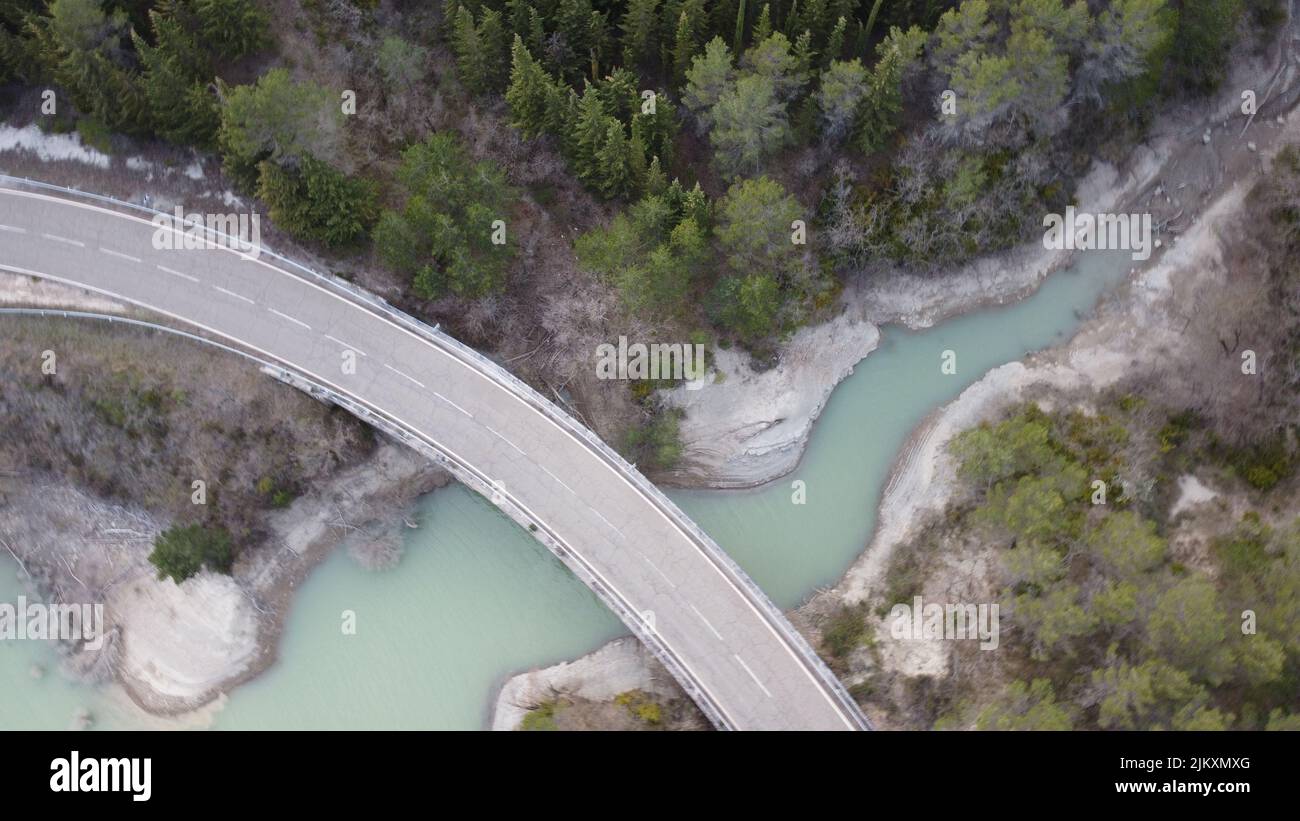 An areal view of a bridge passes over the river and green trees on both sides in daylight Stock Photo