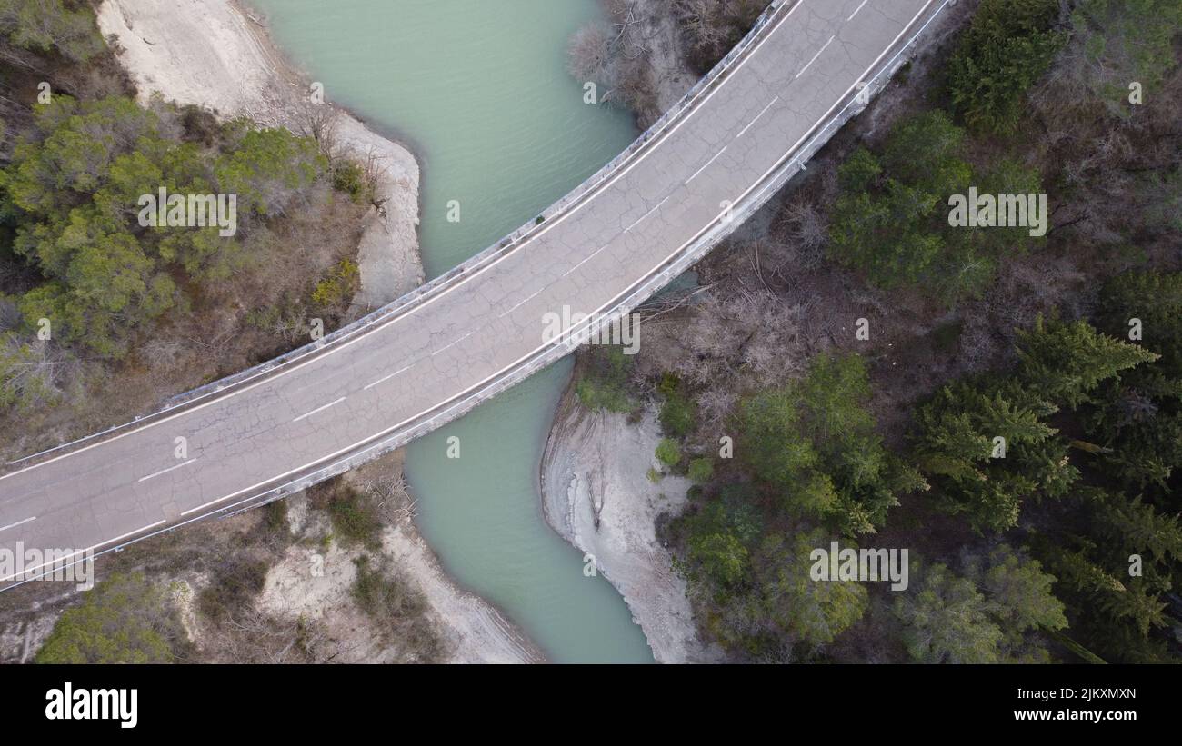 An areal view of a bridge passes over the river and green trees on both sides in daylight Stock Photo