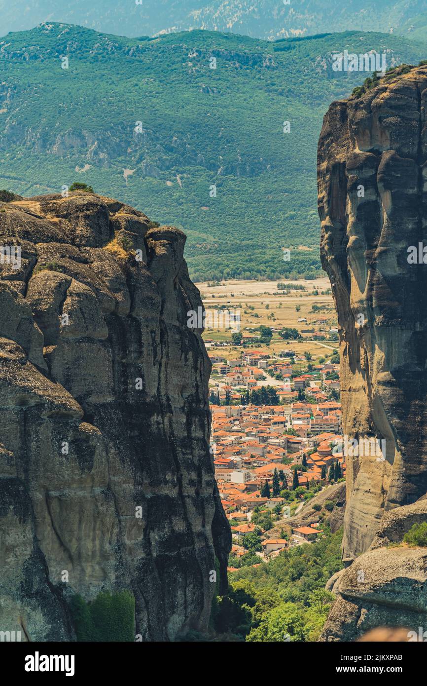 Vertical shot of the gap between two rock formations of Meteora and the city of Kalambaka peeking through. Diversity of Greek landscape. High quality photo Stock Photo
