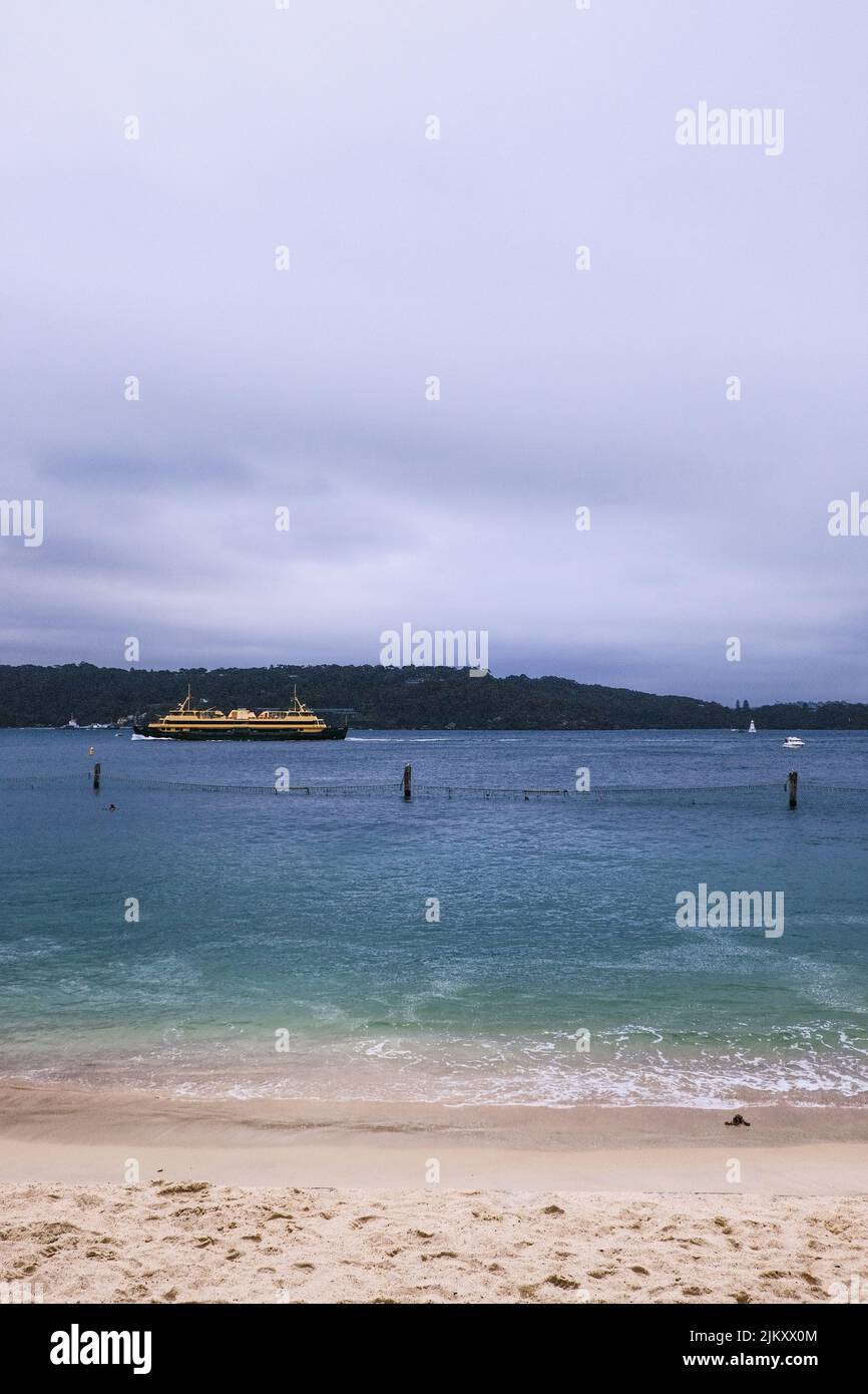 A vertical distant view of a ferry passing by the beach of the Nielson Park, Sydney, Australia Stock Photo