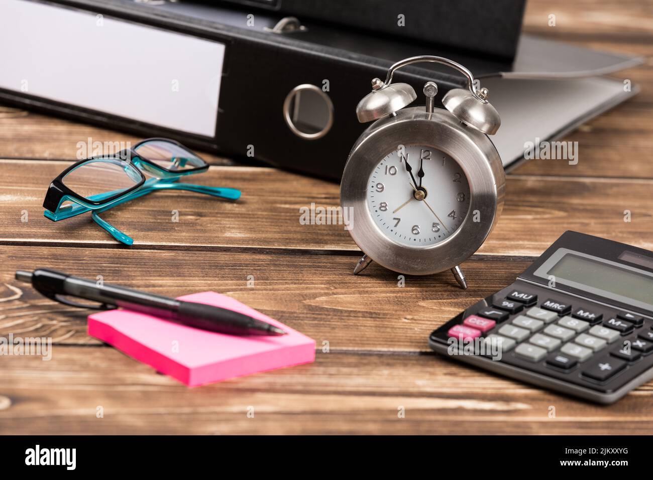 An office desk with a clock, calculator, glasses, and folders Stock