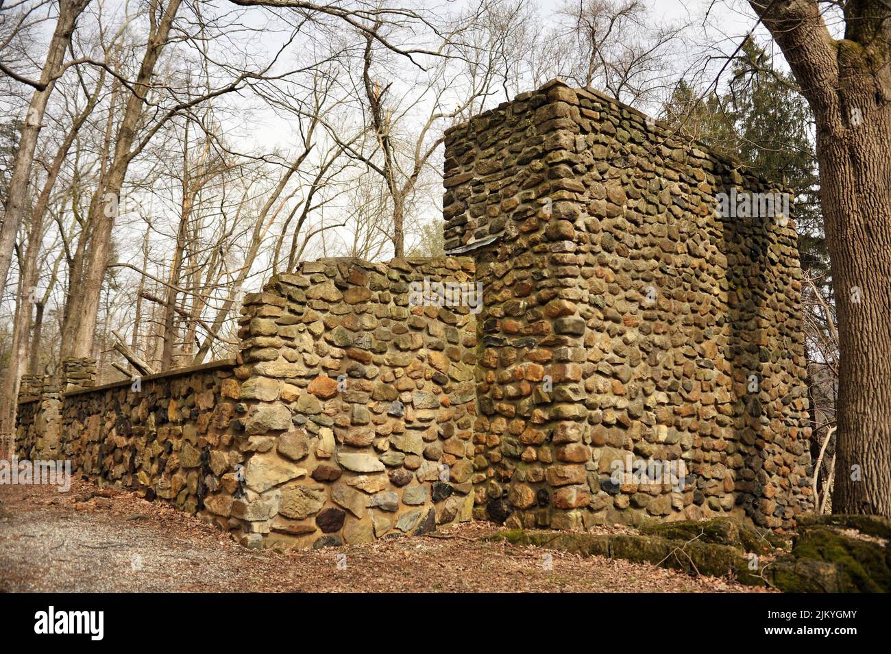 A stone wall surrounded by leafless trees against cloudy sky on a sunny day in Kittatinny Valley State Park, New Jersey, United States Stock Photo