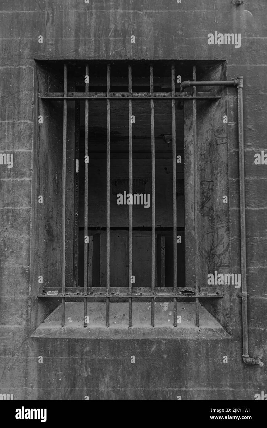 A grayscale shot of a an open window with metal bars on it in an old ...