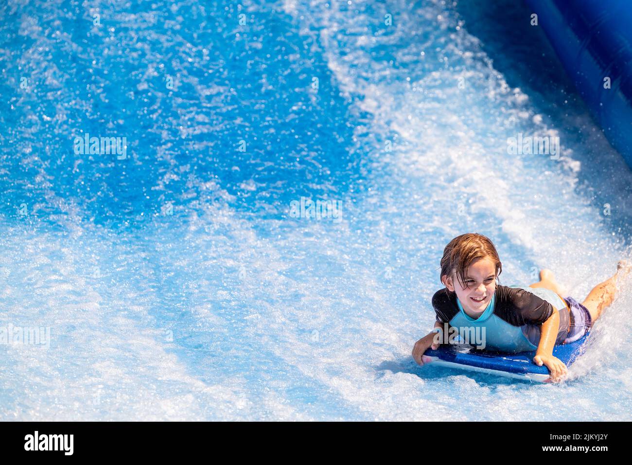 Kids playing at a Public Pool riding the FlowRider, jumping off diving