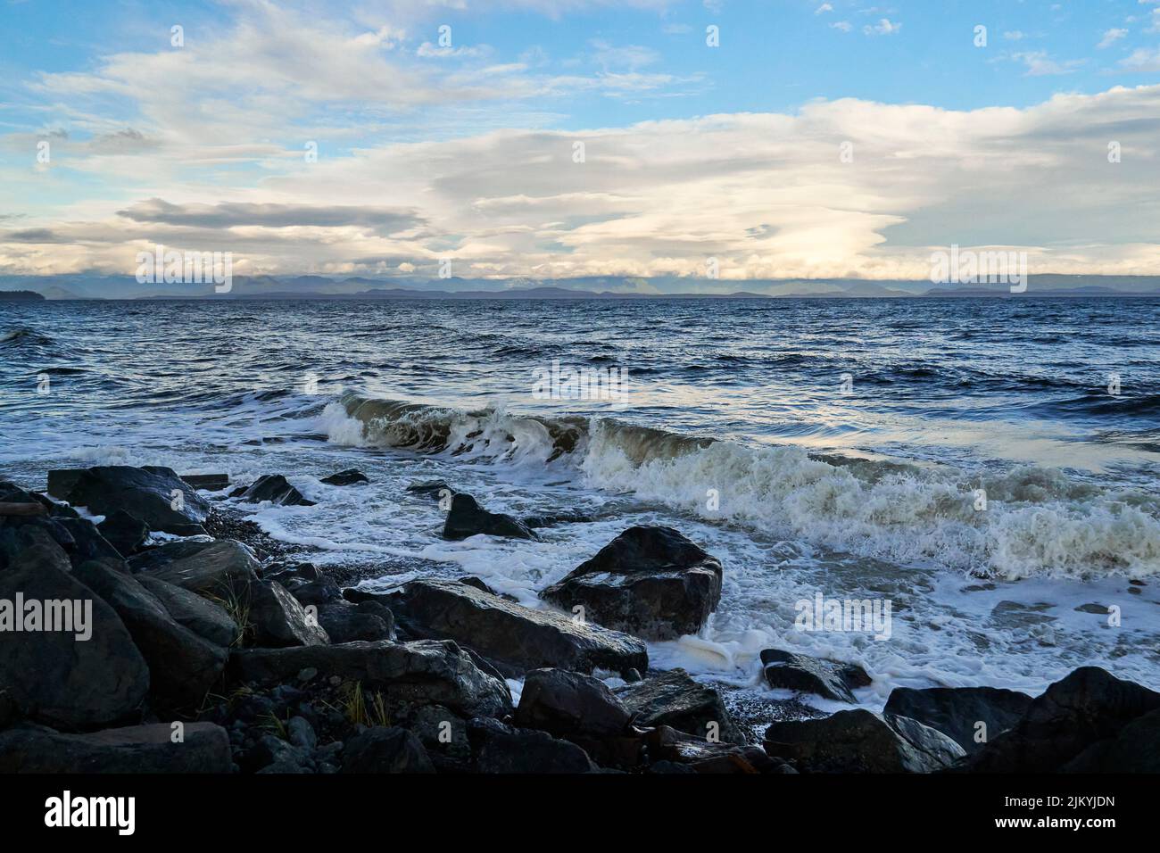 A stormy winter day at an ocean beach. Waves crashing into the dark rocky beach. Stock Photo