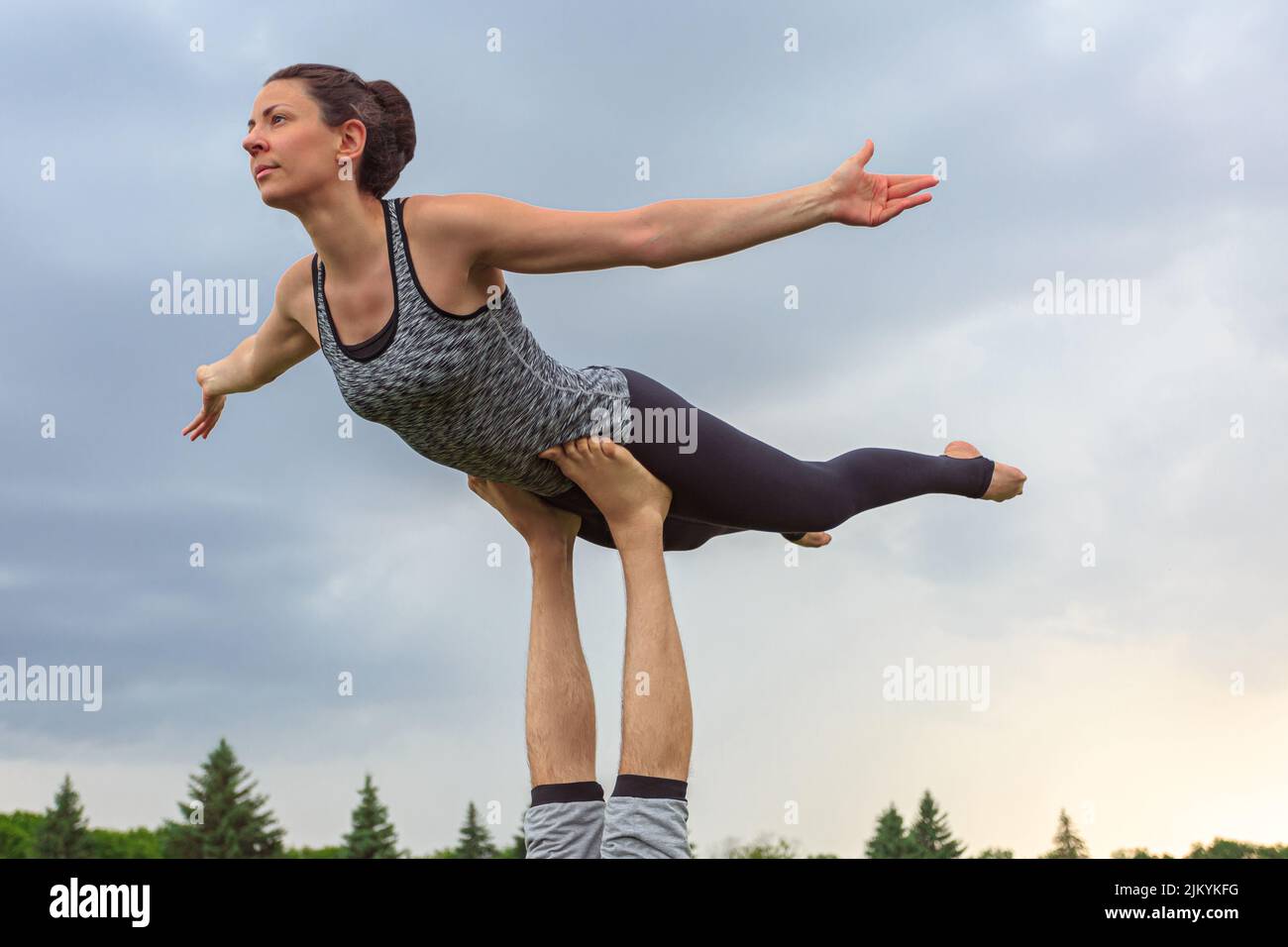 Close up of man lying on grass and balancing woman in his feet. Young couple doing acro yoga in park Stock Photo