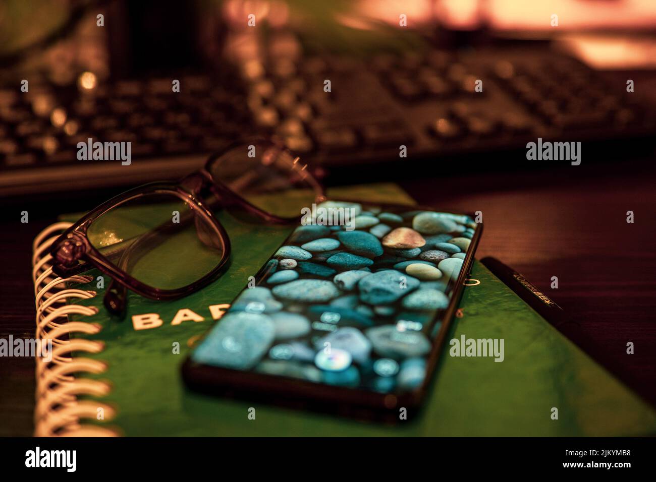 A closeup shot of a Samsung s9 and eyeglasses on a green notebook on a brown table in an office in Nairobi, Kenya Stock Photo