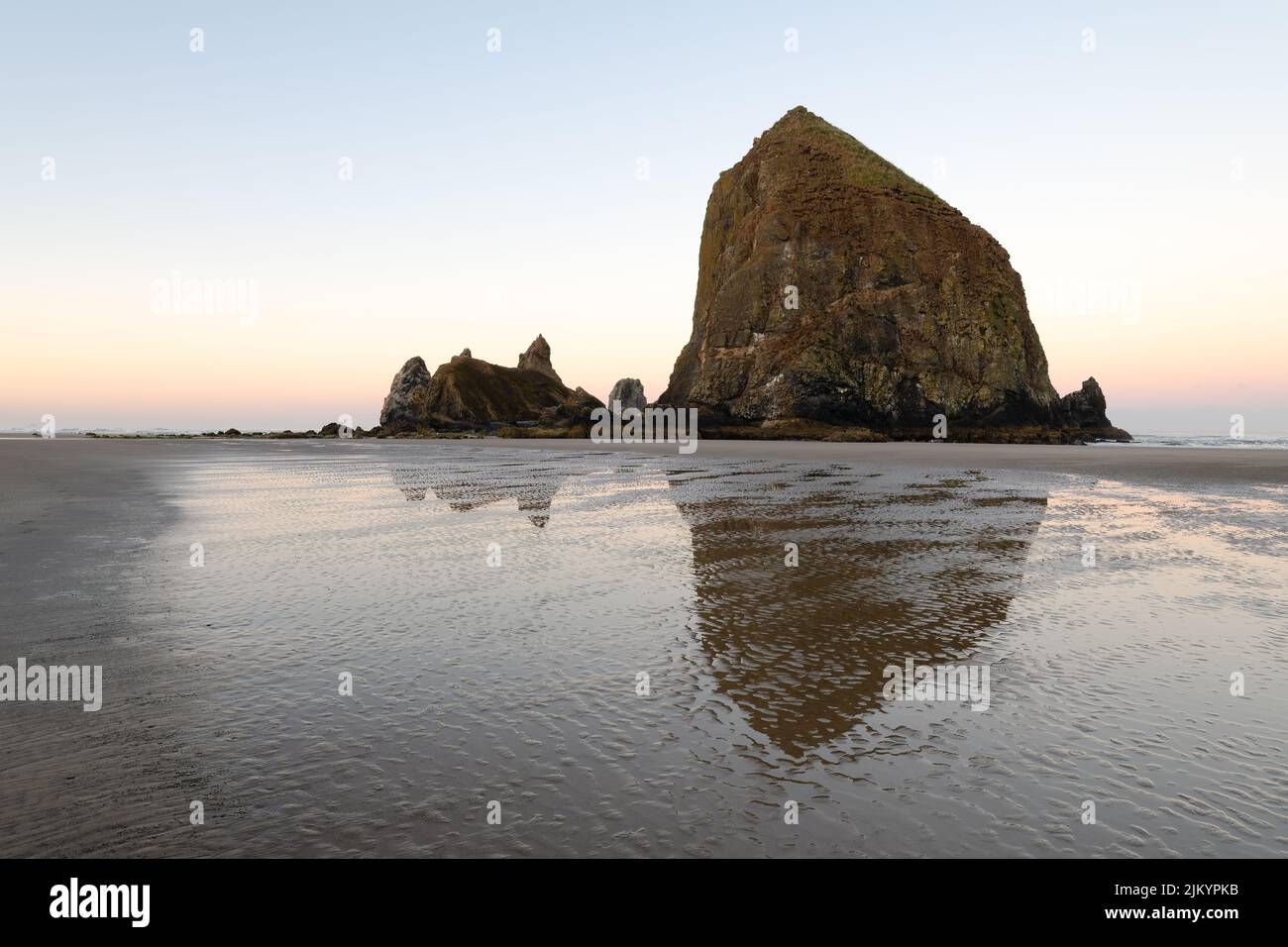 Dawn at monolith Haystack Rock at Cannon Beach Oregon with a reflection in wet sand with ripples in the early morning Stock Photo