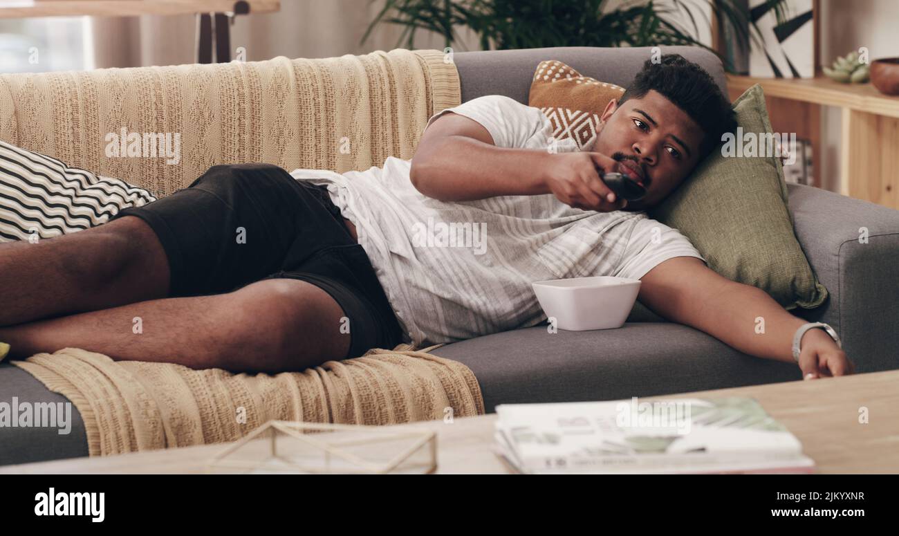 Finally my favourite TV show is on. a young man lying on his couch at home. Stock Photo