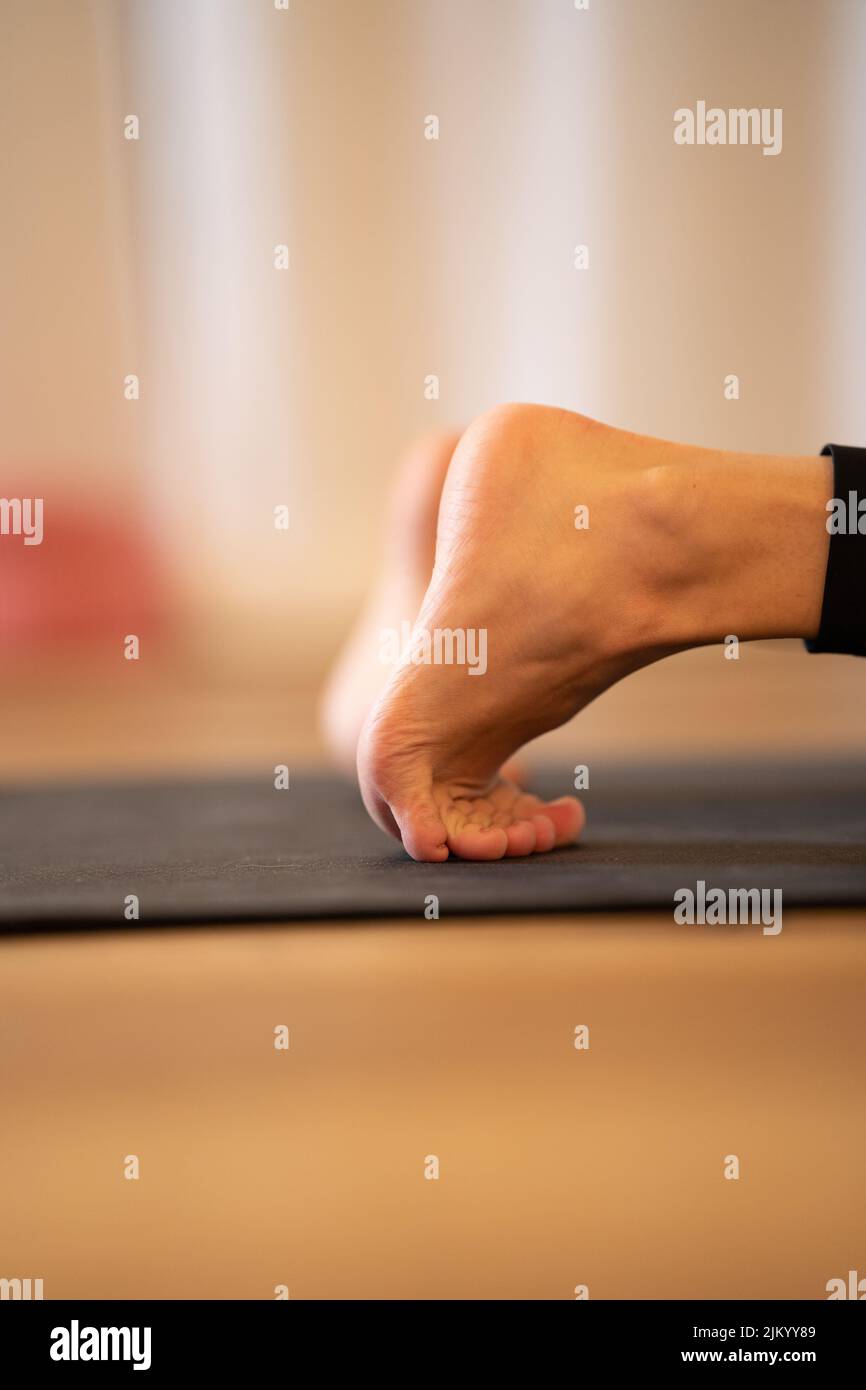 A vertical shot of human legs doing yoga exercise on mat Stock Photo
