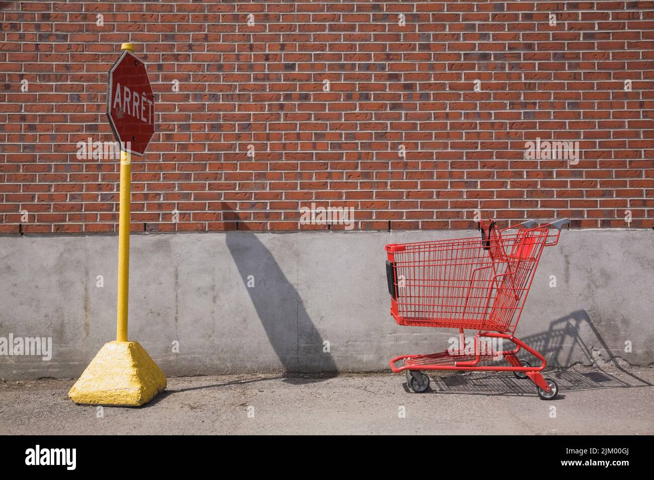 Abandoned red shopping cart in front of French language stop sign