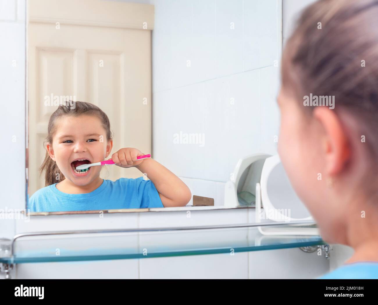 Girl brushing her teeth looking in the mirror in the restroom Stock