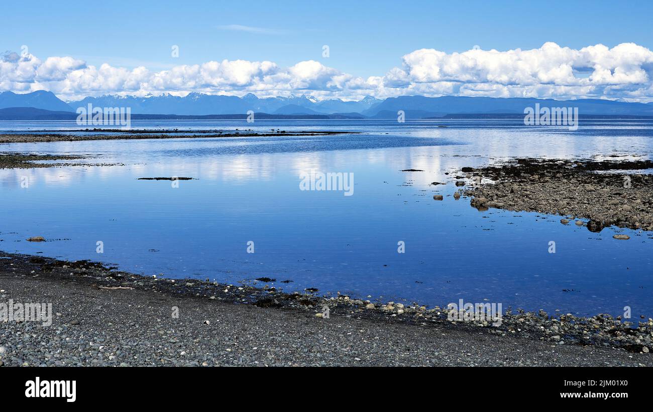 Ocean view from a rocky beach of the beautiful, calm deep blue water and the distant fluffy clouds on a bright summer day. Stock Photo