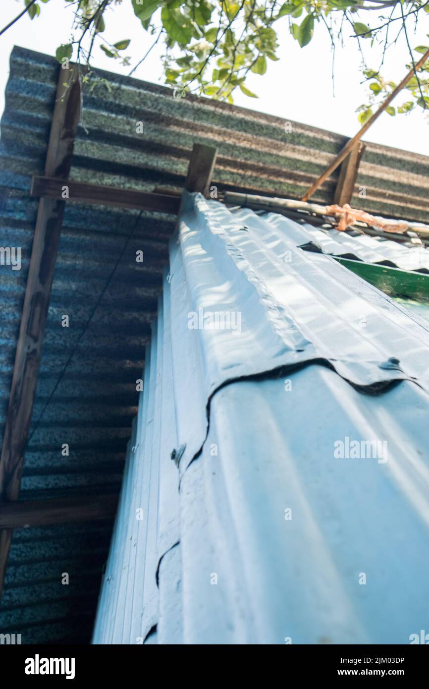 A bottom-up photo of a corner of a village house made of GCI sheets. The roof of the house is also made of GCI sheets. Stock Photo